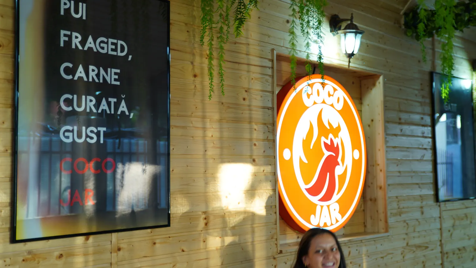 Perete din lemn cu mesajul Coco Jar și logo-ul iluminat al restaurantului